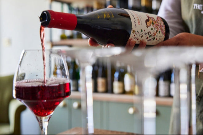 Person pouring red wine into a glass with a Maltings branded apron in the background